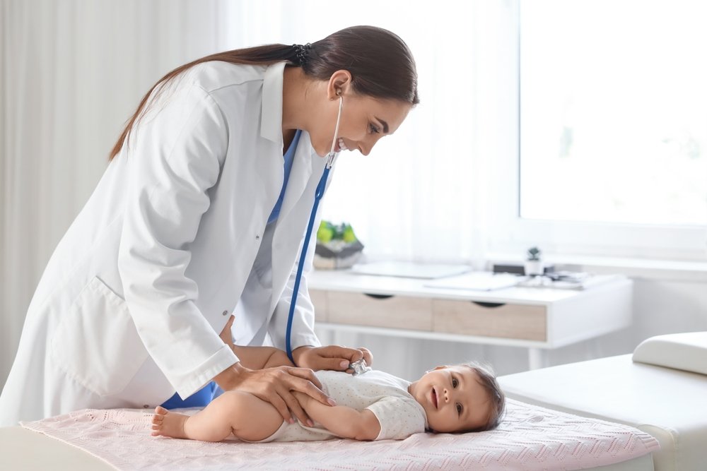 Female,Pediatrician,With,Stethoscope,Listening,To,Little,Baby,On,Couch